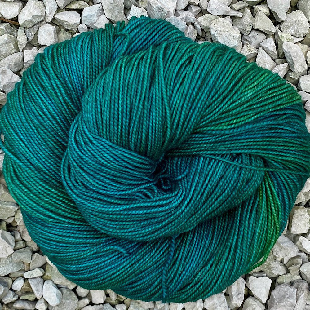 Merino and nylon hand dyed yarn shown in a closed circle swirl. Deep Jungle greens, with yellowish green sections
