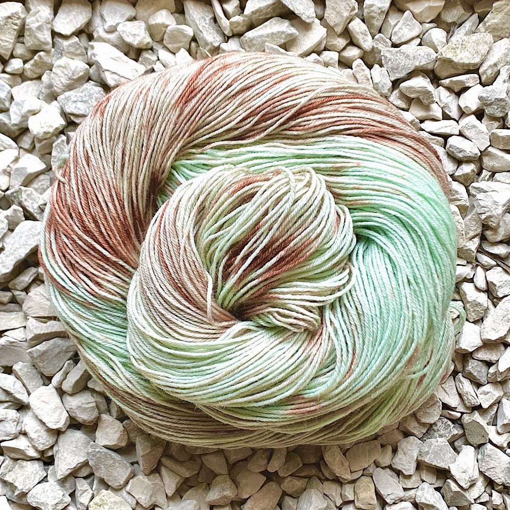 Photo of Hand dyed BFL wool shown swirled into a circle shape on a background of pebbles