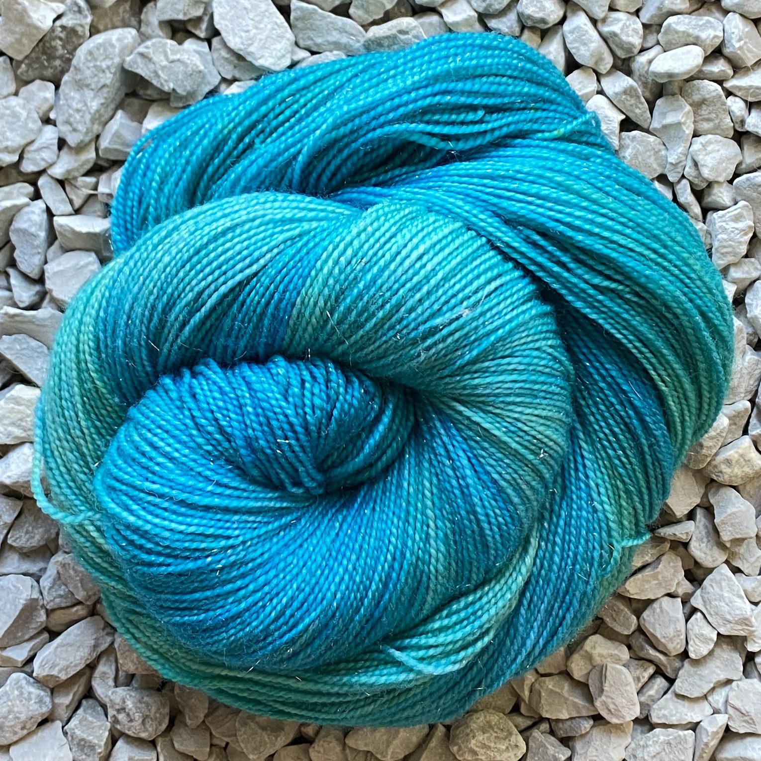 A Swirl of sparkly yarn hand-dyed in a blend of sea greens and sea blues