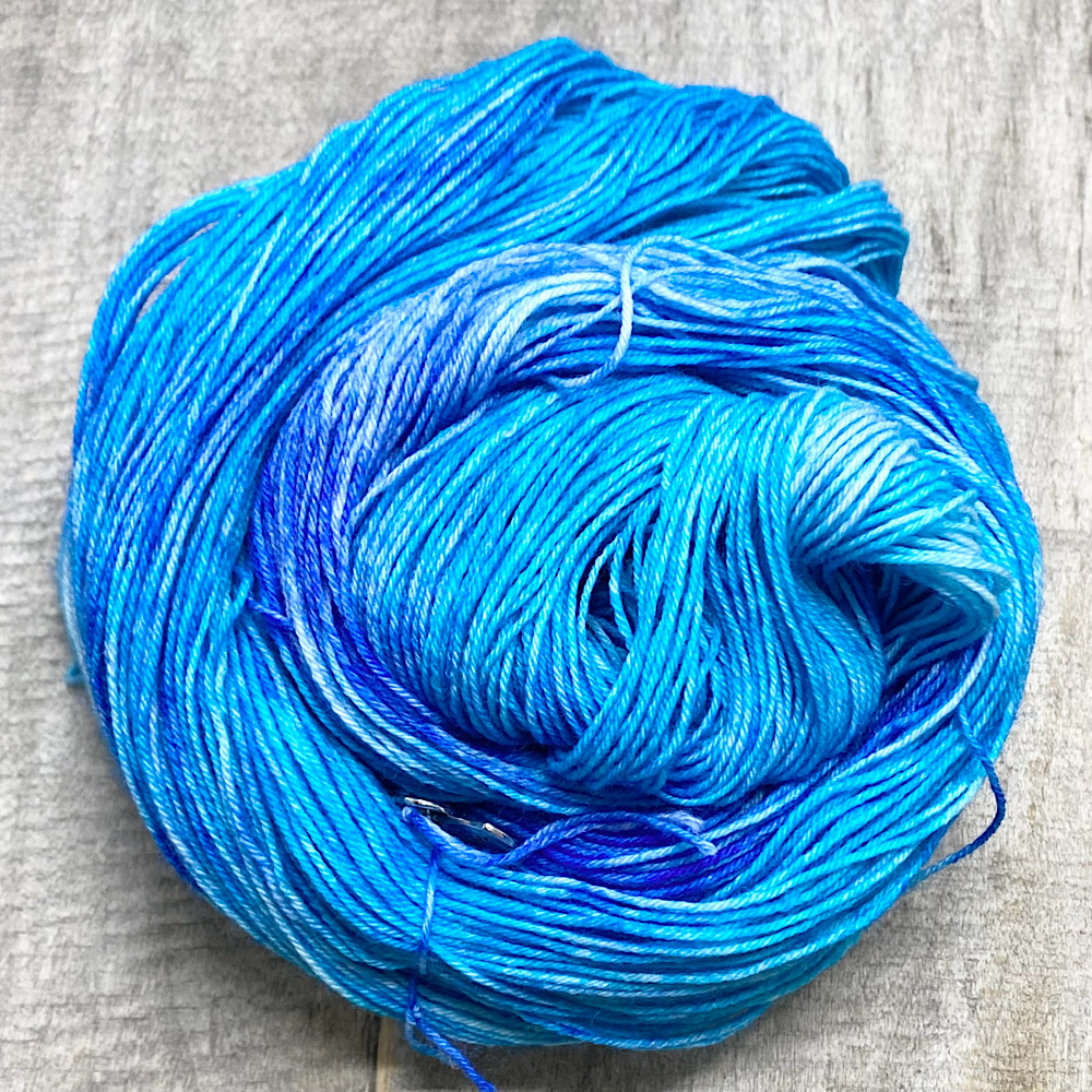 Photograph of hand dyed BFL wool 'Adriatic', arranged in a swirl. The colours are a range of blues and turquoises.