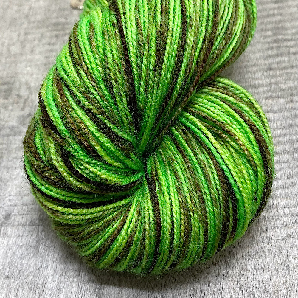 Hand dyed pure BFL wool, spun with a twist, in colour 'Chocolate Lime' - a lome base with painted strands of chocolate colour.. Photo shows a close-up of the end of a skein.