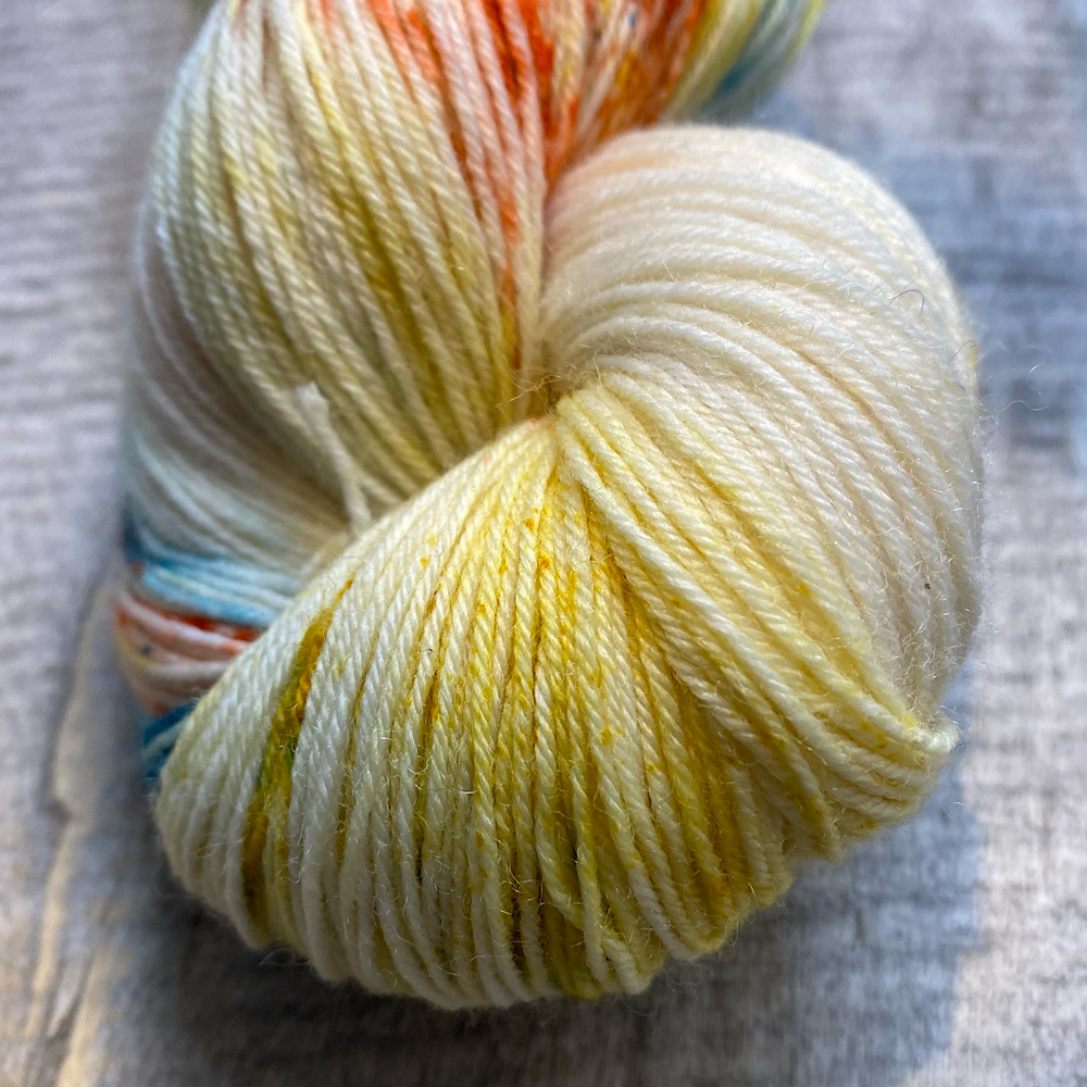 Photograph of hand dyed BFL wool in 'Copper Verdigris', showing a close-up of the end of a skein. The colours are the bare wool with some pale copper toning and sprinkles of Verdigris.