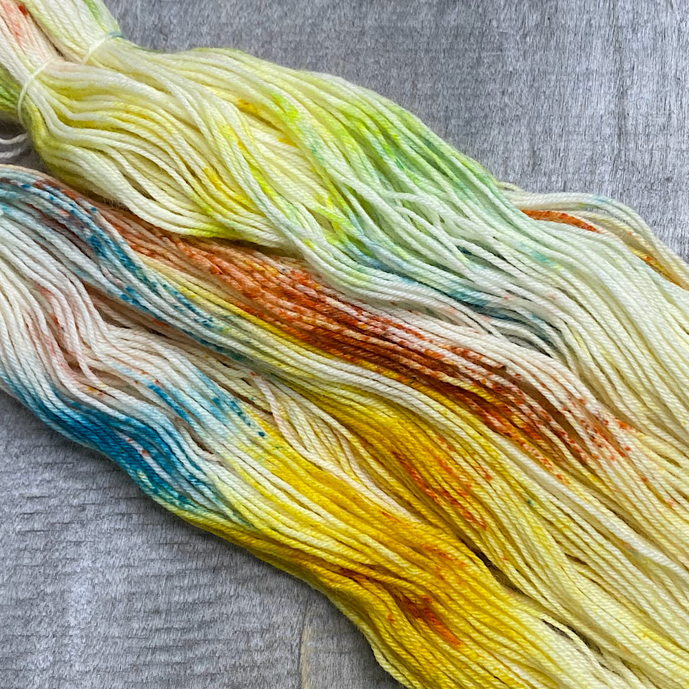 Photograph of hand dyed BFL wool in 'Copper Verdigris', arranged in flat and spread out. The colours are a mix of copper tones and the Verdigris colours of outdoor copper..