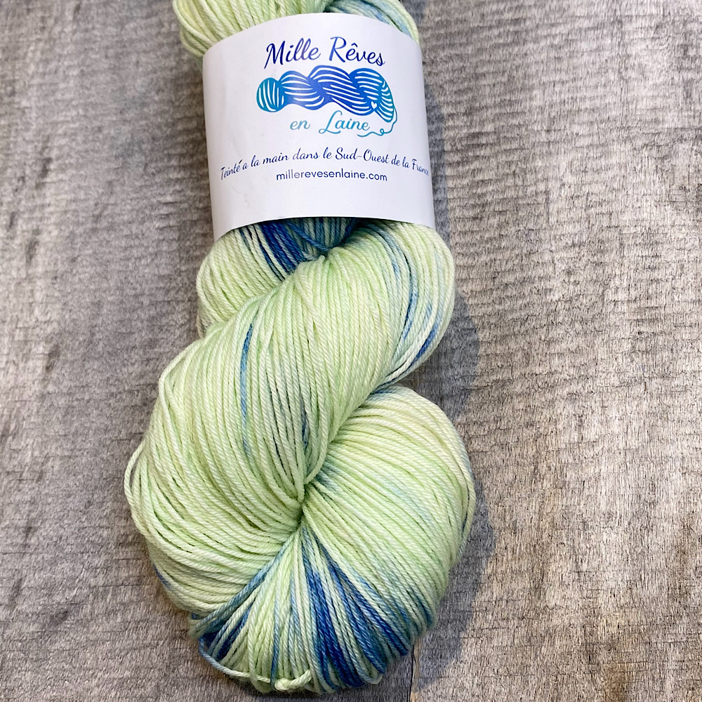 A portion of a skein of hand dyed wool in colour, 'East Beach'. A pale green/yellow background with blue dye painted through.