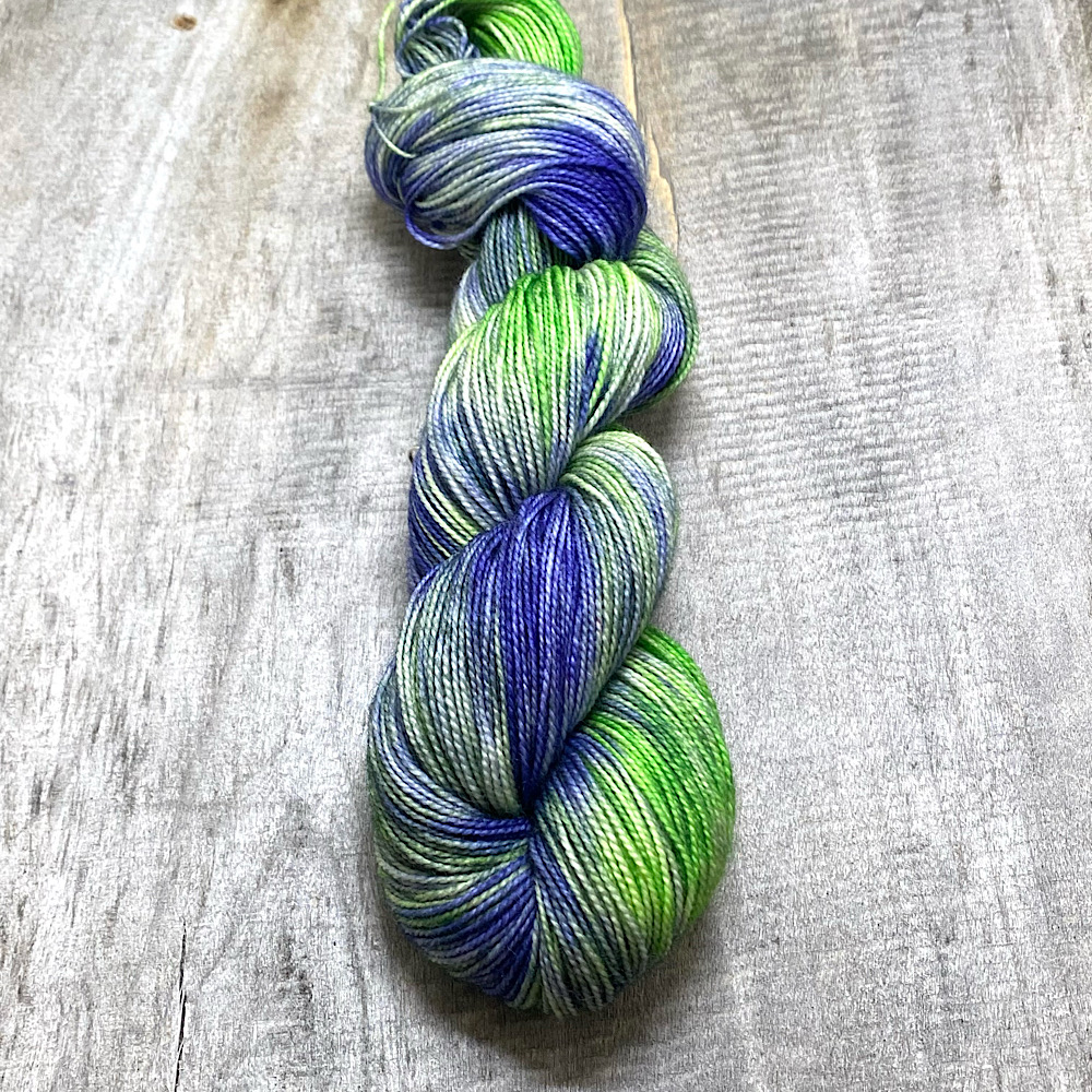 A skein of hand dyed pure BFL wool, spun with a twist, in colour 'Lavender Field'. A variegated dye style in a deep green and lavender colours.