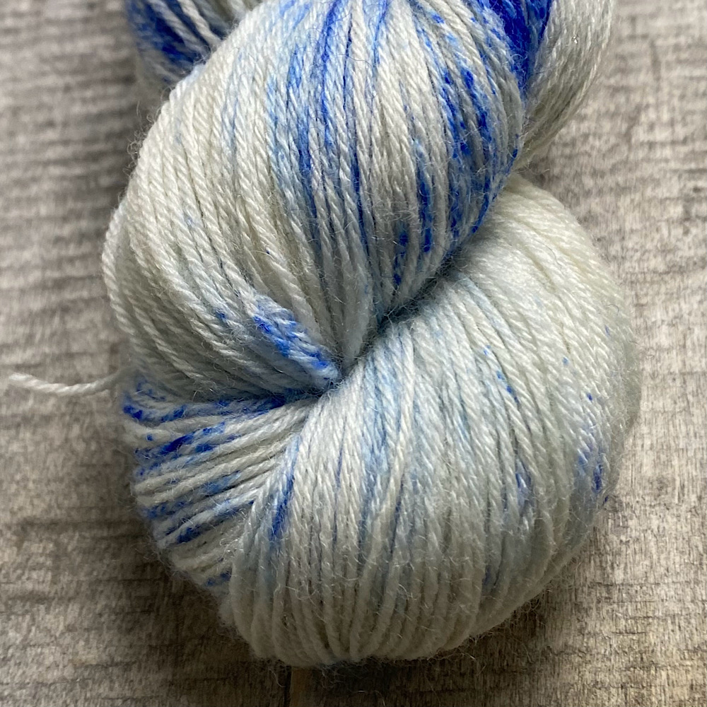 Photograph of hand dyed BFL wool in 'Sailor Moon', showing a close-up of the end of a skein. The blue is sprinkled on the bare wool in powder form.