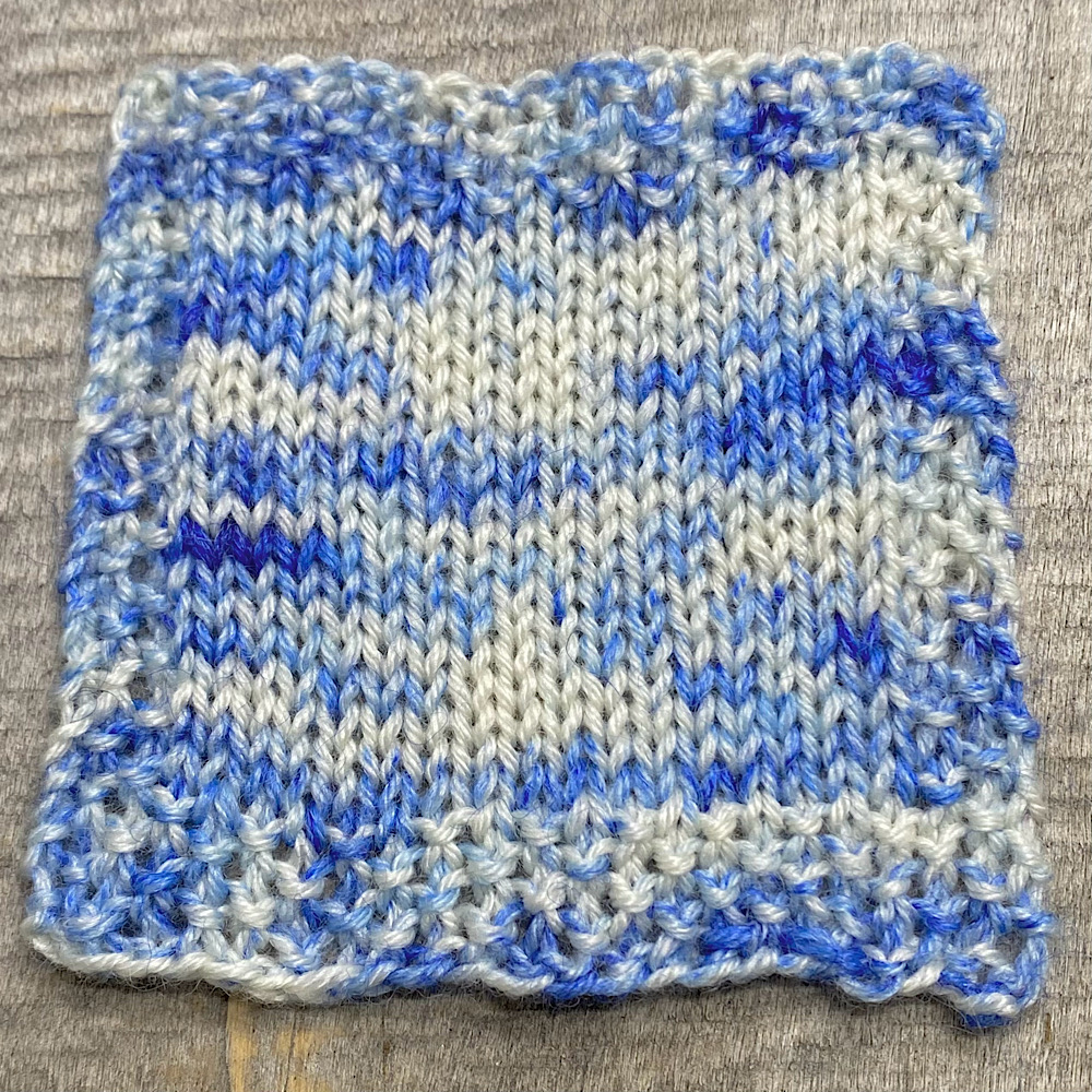 Photograph of a knitted square in hand dyed BFL wool in 'Sailor Moon', showing the blue sprinkles and the general look of the dye style.