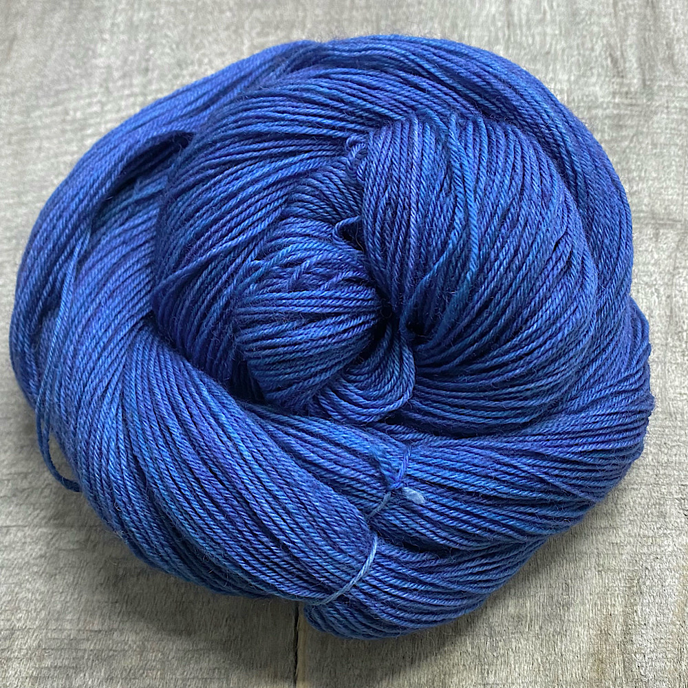 Photograph of hand dyed BFL wool in 'Copper Verdigris', arranged in a swirl. The colours are a mix of mid to deep blues, which have a hint of grey.