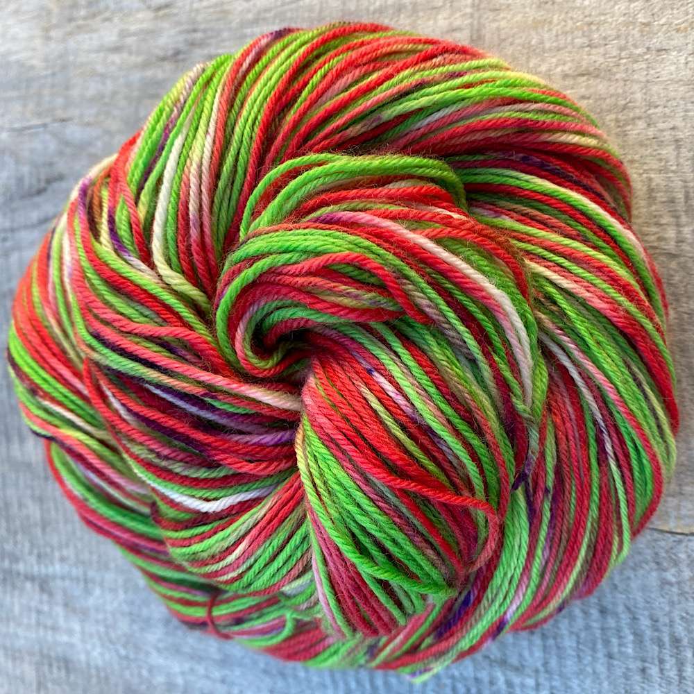 A swirled, variegated skein of hand dyed yarn in reds and greens