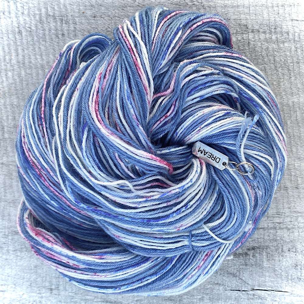 A swirl of hand dyed yarn called 'Deauville' in denim blue with speckles of darker blue and deep pink. there are strands of natural wool showing through.